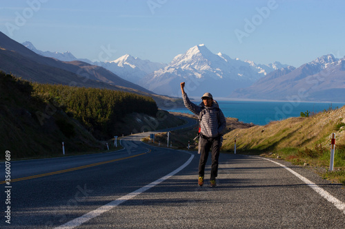 Travel man hitchhiking. A hitchhiker by the road during vacation trip in New Zealand with mountains in the background. The concept of traveling and hitchhiking.