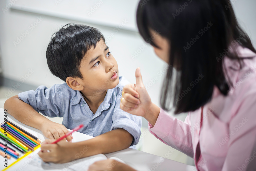 Asian female teacher teaching kid writing lesson and reading book in classroom, Special education during school holidays. Asian female teacher teaching kid writing lesson and reading book in classroom, Special education during school holidays.