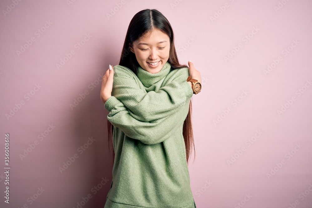 Young beautiful asian woman wearing green winter sweater over pink solated background Hugging oneself happy and positive, smiling confident. Self love and self care Young beautiful asian woman wearing green winter sweater over pink solated background Hugging oneself happy and positive, smiling confident. Self love and self care