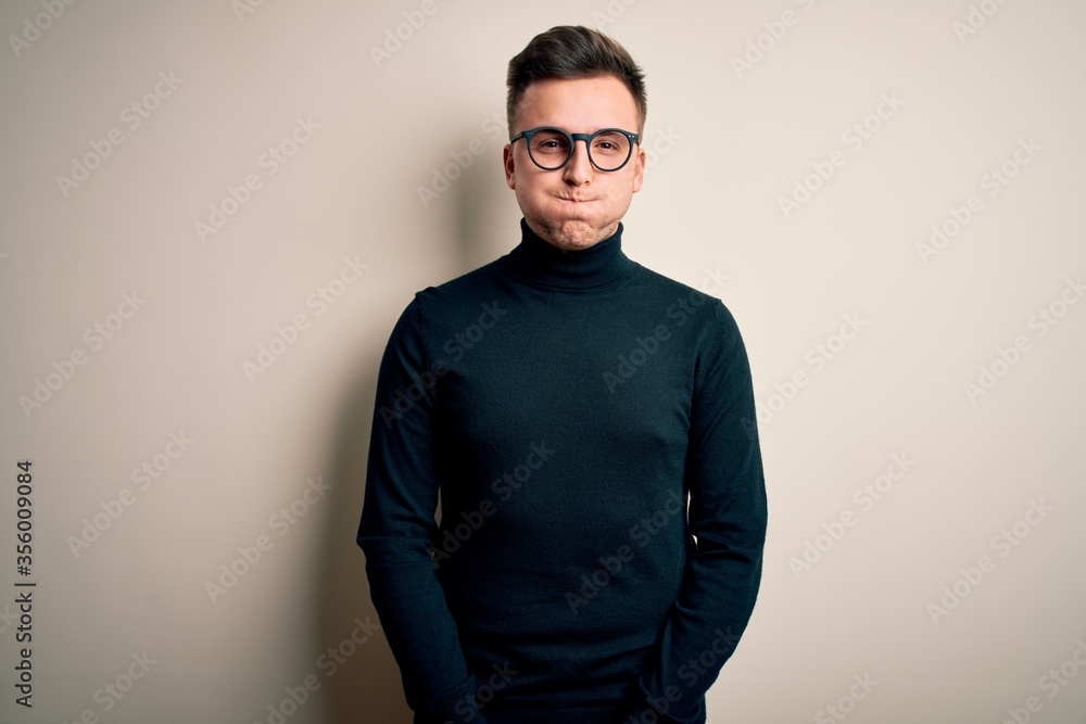 Young handsome caucasian man wearing glasses and casual sweater over isolated background puffing cheeks with funny face. Mouth inflated with air, crazy expression. Young handsome caucasian man wearing glasses and casual sweater over isolated background puffing cheeks with funny face. Mouth inflated with air, crazy expression.