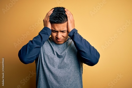 Young handsome latin man wearing casual t-shirt standing over yellow background suffering from headache desperate and stressed because pain and migraine. Hands on head. © Krakenimages.com