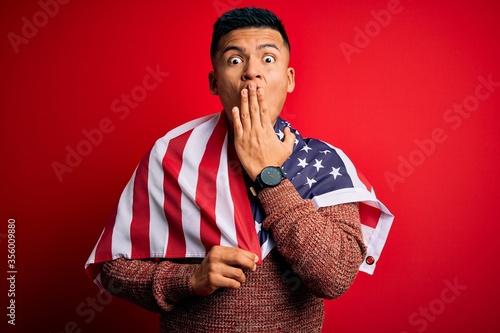 Young handsome latin patriotic man wearing united states of america falg cover mouth with hand shocked with shame for mistake, expression of fear, scared in silence, secret concept photo