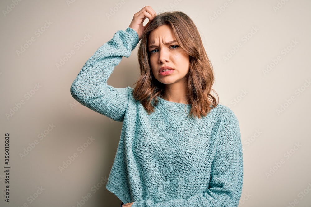 Young blonde girl wearing casual blue winter sweater over isolated background confuse and wonder about question. Uncertain with doubt, thinking with hand on head. Pensive concept. Young blonde girl wearing casual blue winter sweater over isolated background confuse and wonder about question. Uncertain with doubt, thinking with hand on head. Pensive concept.