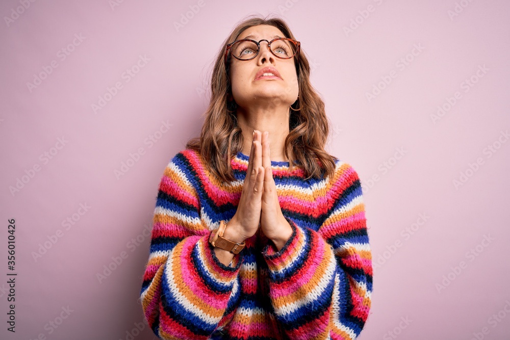 Young beautiful blonde girl wearing glasses and casual sweater over pink isolated background begging and praying with hands together with hope expression on face very emotional and worried. Begging. Young beautiful blonde girl wearing glasses and casual sweater over pink isolated background begging and praying with hands together with hope expression on face very emotional and worried. Begging.