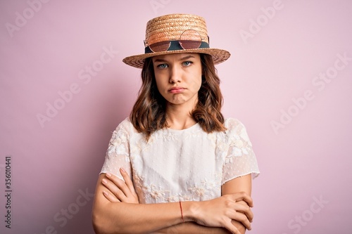 Young beautiful blonde girl wearing summer hat over pink isolated background skeptic and nervous, disapproving expression on face with crossed arms. Negative person.