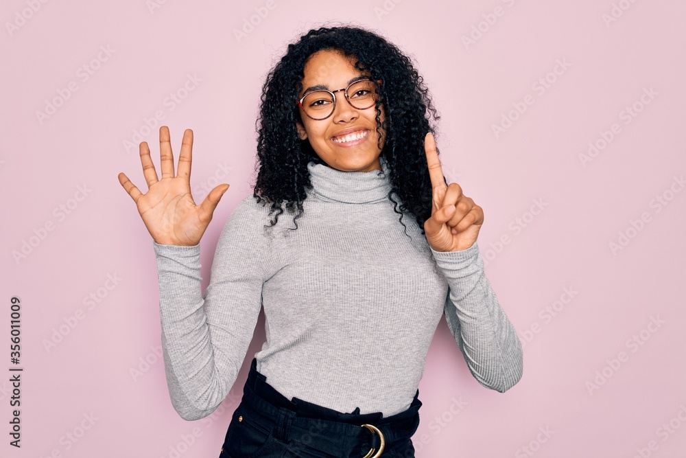 Young african american woman wearing turtleneck sweater and glasses over pink background showing and pointing up with fingers number six while smiling confident and happy. Young african american woman wearing turtleneck sweater and glasses over pink background showing and pointing up with fingers number six while smiling confident and happy.