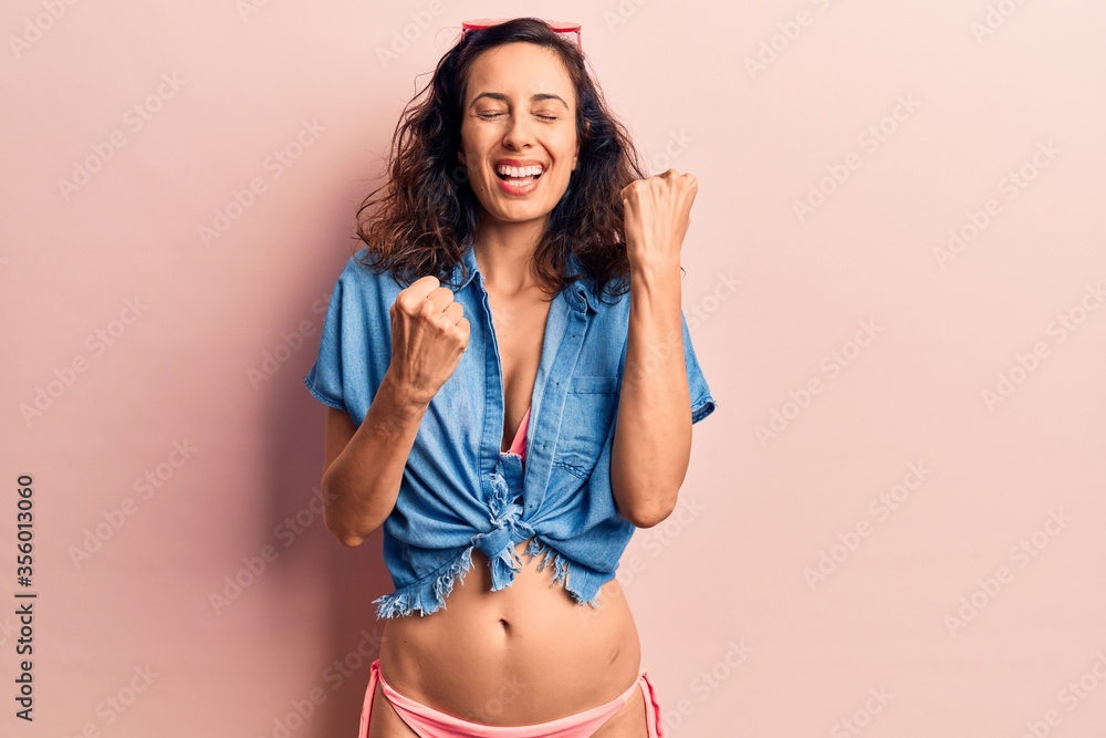 Fototapeta premium Young beautiful hispanic woman wearing bikini and shirt celebrating surprised and amazed for success with arms raised and eyes closed