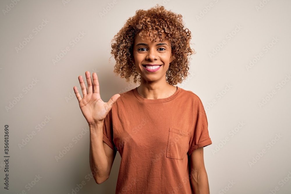 Beautiful african american woman with curly hair wearing casual t-shirt over white background showing and pointing up with fingers number five while smiling confident and happy. Beautiful african american woman with curly hair wearing casual t-shirt over white background showing and pointing up with fingers number five while smiling confident and happy.