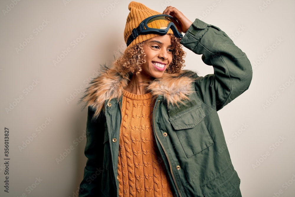 Young african american skier woman with curly hair wearing snow sportswear and ski goggles smiling confident touching hair with hand up gesture, posing attractive and fashionable Young african american skier woman with curly hair wearing snow sportswear and ski goggles smiling confident touching hair with hand up gesture, posing attractive and fashionable