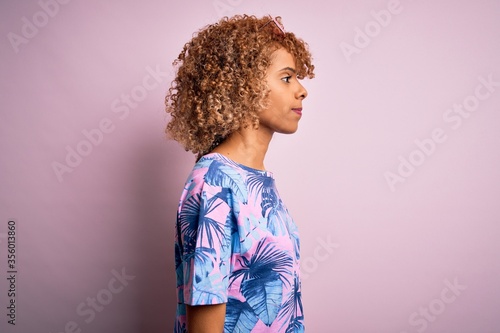 Young african american woman on vacation wearing summer t-shirt over pink background looking to side, relax profile pose with natural face with confident smile.