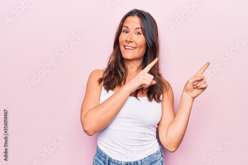 Young beautiful brunette woman wearing casual sleeveless t-shirt over white background smiling and looking at the camera pointing with two hands and fingers to the side. © Krakenimages.com