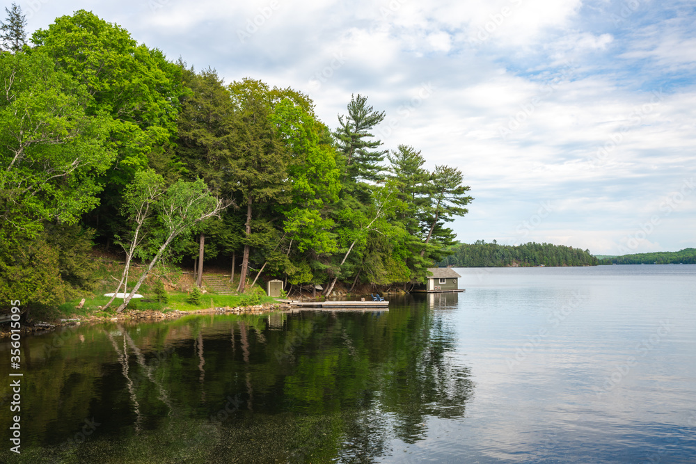 Beautiful View of Lake in Muskoka during Clear Summer Weather with reflection in water and small shed Beautiful View of Lake in Muskoka during Clear Summer Weather with reflection in water and small shed
