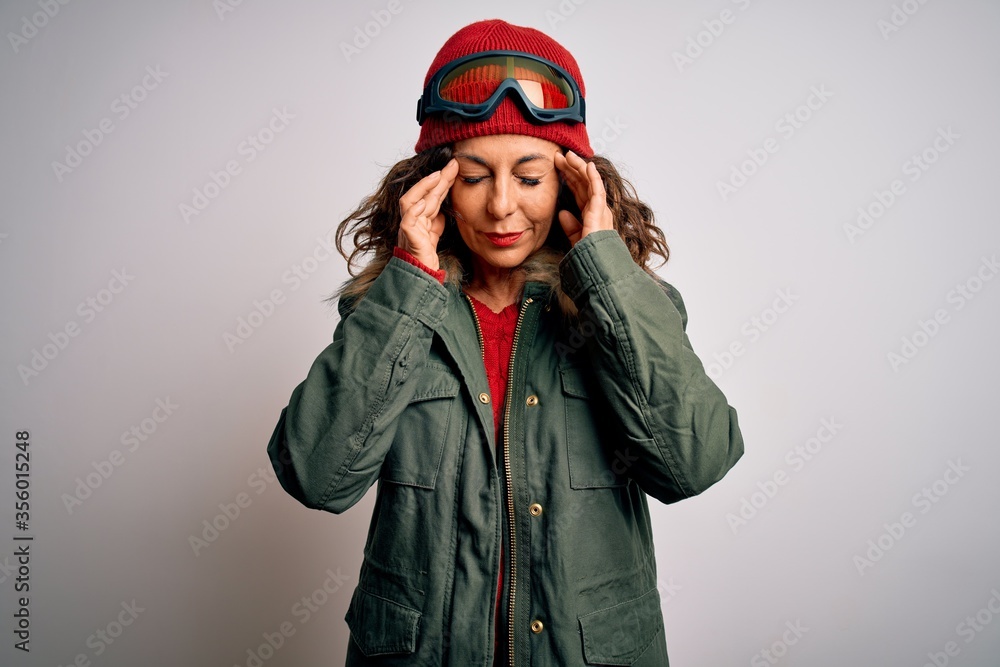 Middle age skier woman wearing snow sportswear and ski goggles over white background with hand on head for pain in head because stress. Suffering migraine.