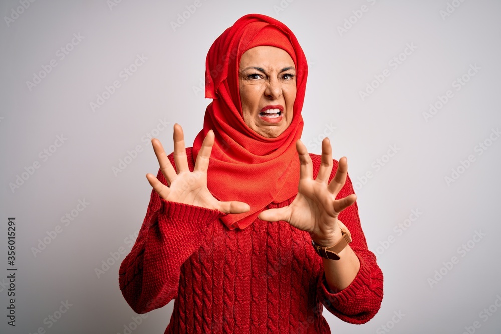 Middle age brunette woman wearing muslim traditional hijab over isolated white background afraid and terrified with fear expression stop gesture with hands, shouting in shock. Panic concept. Middle age brunette woman wearing muslim traditional hijab over isolated white background afraid and terrified with fear expression stop gesture with hands, shouting in shock. Panic concept.