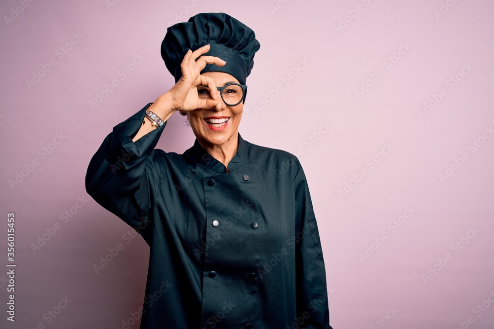 Middle age brunette chef woman wearing cooker uniform and hat over isolated pink background doing ok gesture with hand smiling, eye looking through fingers with happy face. Middle age brunette chef woman wearing cooker uniform and hat over isolated pink background doing ok gesture with hand smiling, eye looking through fingers with happy face.