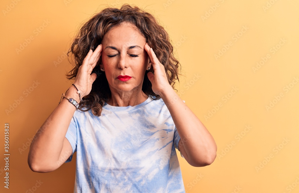 Middle age beautiful woman wearing casual dye t-shirt standing over yellow background with hand on head, headache because stress. Suffering migraine. Middle age beautiful woman wearing casual dye t-shirt standing over yellow background with hand on head, headache because stress. Suffering migraine.