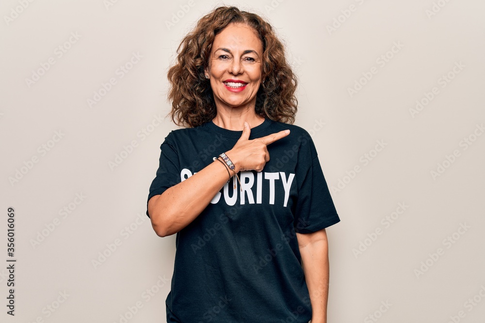 Middle age beautiful guard woman wearing security t-shirt uniform over white background smiling cheerful pointing with hand and finger up to the side Middle age beautiful guard woman wearing security t-shirt uniform over white background smiling cheerful pointing with hand and finger up to the side