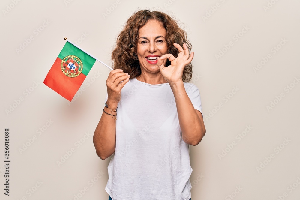 Naklejka premium Middle age beautiful patriotic woman holding portuguese flag over isolated white background doing ok sign with fingers, smiling friendly gesturing excellent symbol