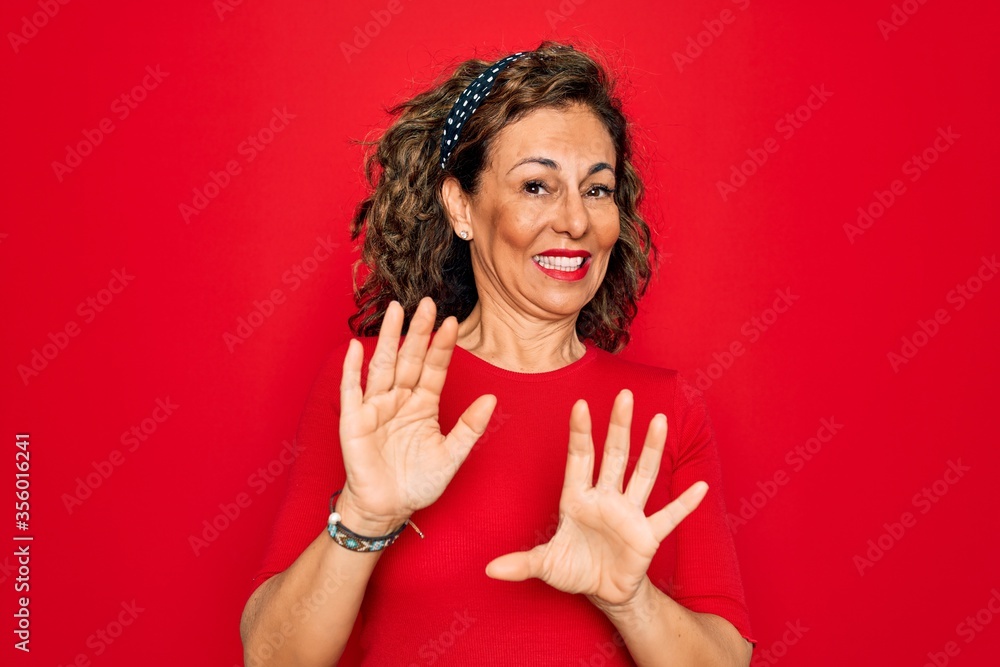 Middle age senior brunette woman wearing casual t-shirt standing over red background disgusted expression, displeased and fearful doing disgust face because aversion reaction. With hands raised Middle age senior brunette woman wearing casual t-shirt standing over red background disgusted expression, displeased and fearful doing disgust face because aversion reaction. With hands raised