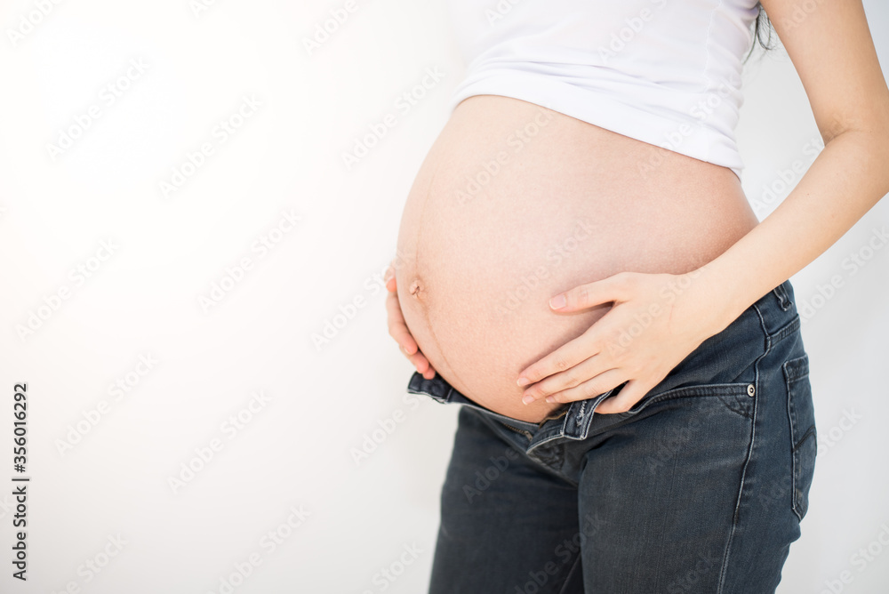 Pregnant woman trying to wear her jeans closeup Pregnant woman trying to wear her jeans closeup