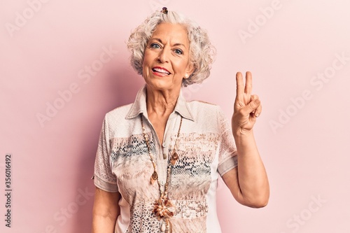Senior grey-haired woman wearing casual clothes smiling with happy face winking at the camera doing victory sign. number two.