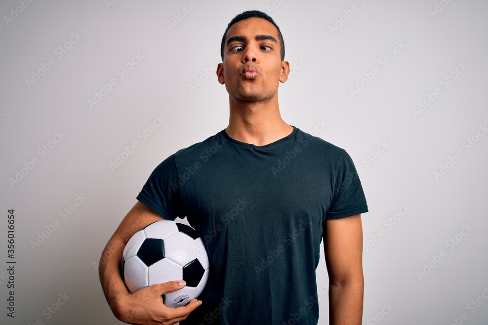 Handsome african american man playing footbal holding soccer ball over white background making fish face with lips, crazy and comical gesture. Funny expression. Handsome african american man playing footbal holding soccer ball over white background making fish face with lips, crazy and comical gesture. Funny expression.