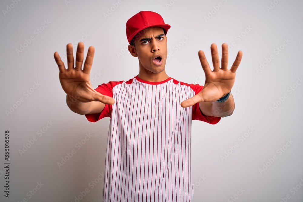 Young handsome african american sportsman wearing striped baseball t-shirt and cap doing stop gesture with hands palms, angry and frustration expression Young handsome african american sportsman wearing striped baseball t-shirt and cap doing stop gesture with hands palms, angry and frustration expression
