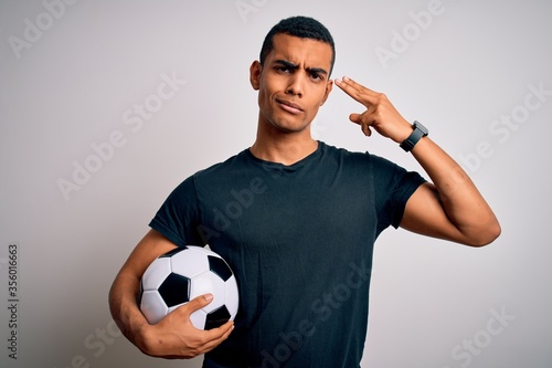 Handsome african american man playing footbal holding soccer ball over white background Shooting and killing oneself pointing hand and fingers to head like gun, suicide gesture.