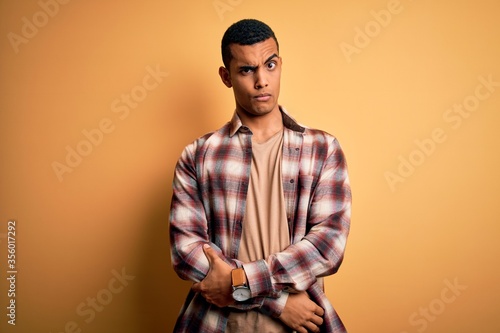 Young handsome african american man wearing casual shirt standing over yellow background skeptic and nervous, frowning upset because of problem. Negative person.