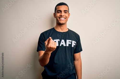 Young handsome african american worker man wearing staff uniform over white background Beckoning come here gesture with hand inviting welcoming happy and smiling © Krakenimages.com