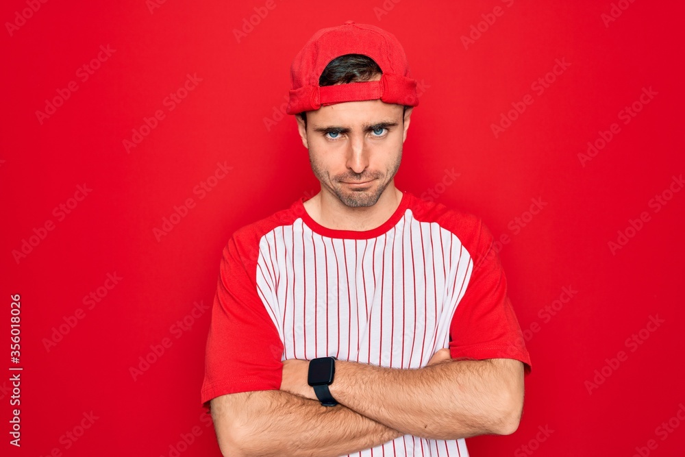 Young handsome sporty man with blue eyes wearing striped baseball t-shirt and cap skeptic and nervous, disapproving expression on face with crossed arms. Negative person. Young handsome sporty man with blue eyes wearing striped baseball t-shirt and cap skeptic and nervous, disapproving expression on face with crossed arms. Negative person.