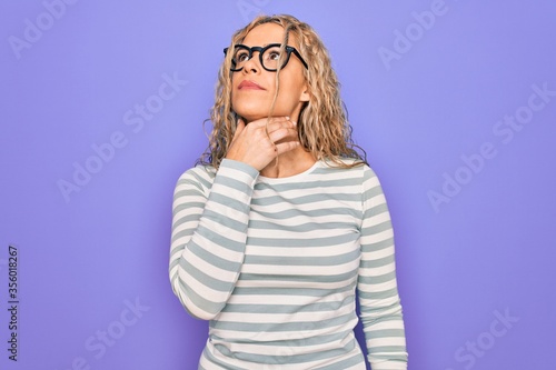 Beautiful blonde woman wearing casual striped t-shirt and glasses over purple background Touching painful neck, sore throat for flu, clod and infection