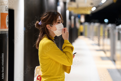 マスクをした女性が地下鉄のホームで電車を待っている