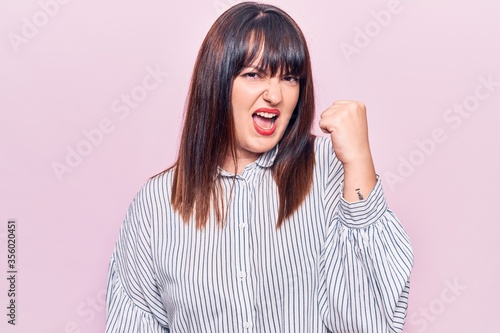 Young plus size woman wearing casual clothes angry and mad raising fist frustrated and furious while shouting with anger. rage and aggressive concept. © Krakenimages.com