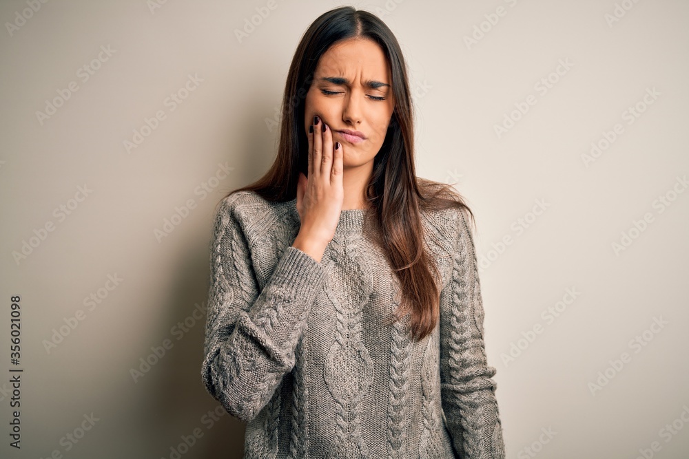Young beautiful brunette woman wearing casual sweater over isolated white background touching mouth with hand with painful expression because of toothache or dental illness on teeth. Dentist Young beautiful brunette woman wearing casual sweater over isolated white background touching mouth with hand with painful expression because of toothache or dental illness on teeth. Dentist