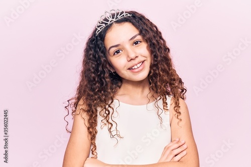 Beautiful kid girl with curly hair wearing princess tiara happy face smiling with crossed arms looking at the camera. positive person.