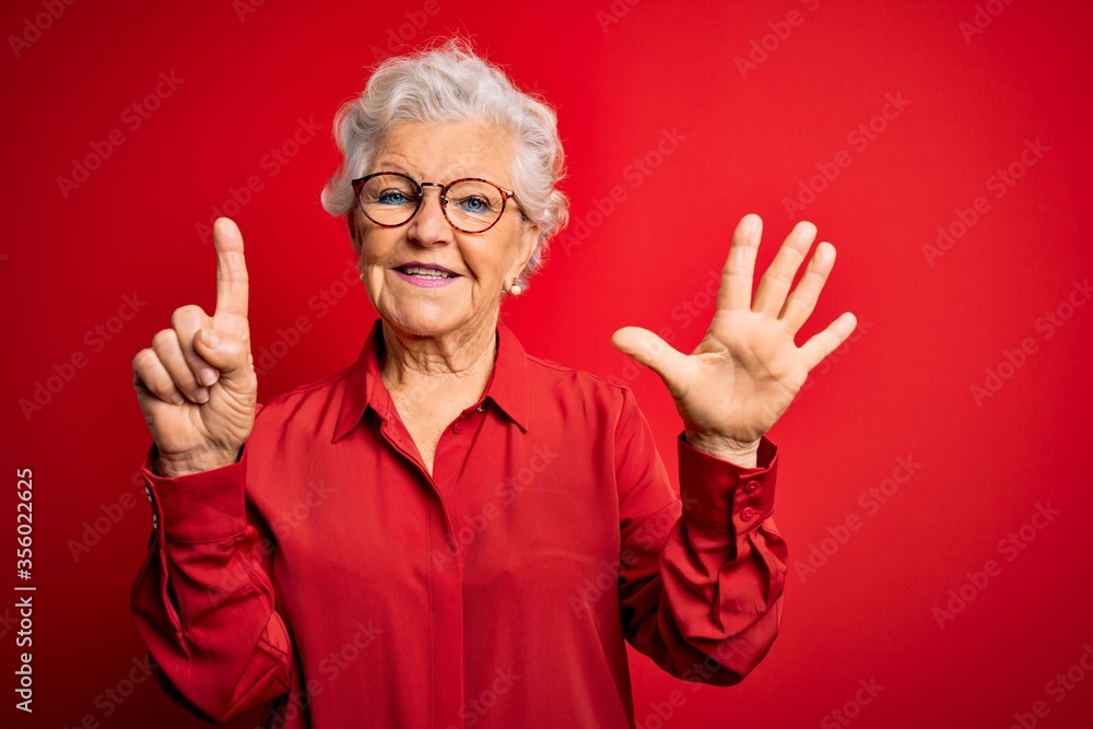 Senior beautiful grey-haired woman wearing casual shirt and glasses over red background showing and pointing up with fingers number six while smiling confident and happy.