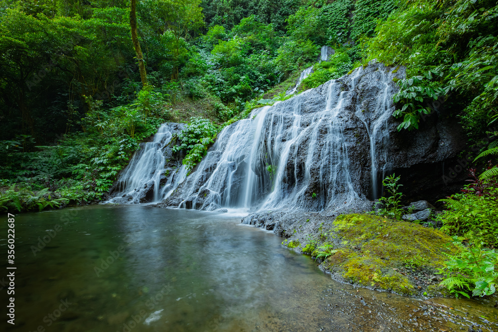 Waterfall landscape. Beautiful hidden waterfall in tropical rainforest. Nature background. Slow shutter speed, motion photography. Pucak Manik waterfall, Bali, Indonesia Waterfall landscape. Beautiful hidden waterfall in tropical rainforest. Nature background. Slow shutter speed, motion photography. Pucak Manik waterfall, Bali, Indonesia