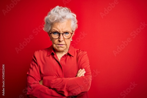 Fotografía Senior beautiful grey-haired woman wearing casual shirt and glasses over red background skeptic and nervous, disapproving expression on face with crossed arms
