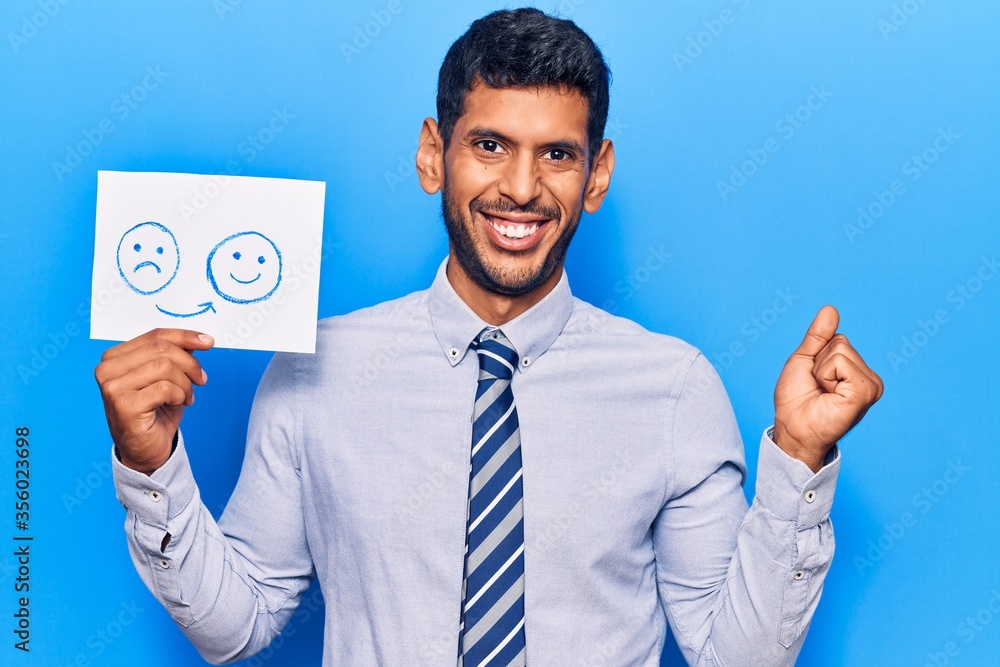 Young latin man holding sad to happy emotion paper celebrating victory with happy smile and winner expression with raised hands