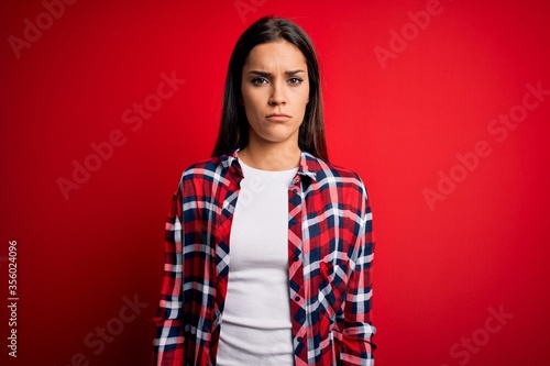 Young beautiful brunette woman wearing casual shirt standing over isolated red background skeptic and nervous, frowning upset because of problem. Negative person. © Krakenimages.com