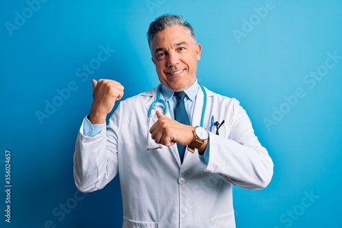 Middle age handsome grey-haired doctor man wearing coat and blue stethoscope Pointing to the back behind with hand and thumbs up, smiling confident