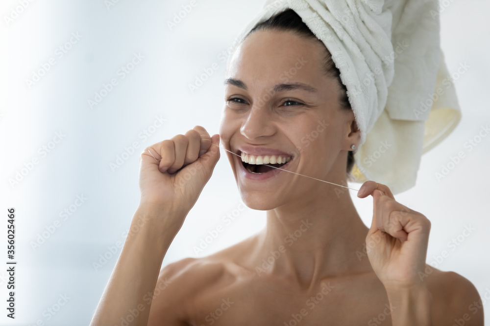 Head shot smiling beautiful woman holding using dental floss, removing food cleaning teeth, standing in bathroom with white bath towel on head, healthcare and personal hygiene, morning routine Head shot smiling beautiful woman holding using dental floss, removing food cleaning teeth, standing in bathroom with white bath towel on head, healthcare and personal hygiene, morning routine