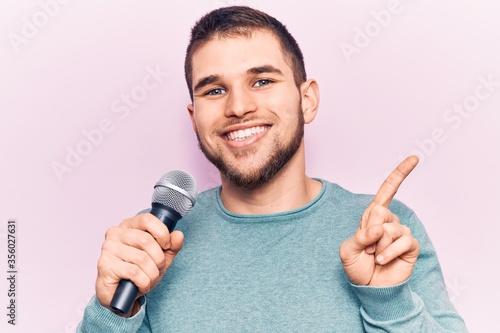 Young handsome man singing song using microphone smiling happy pointing with hand and finger to the side