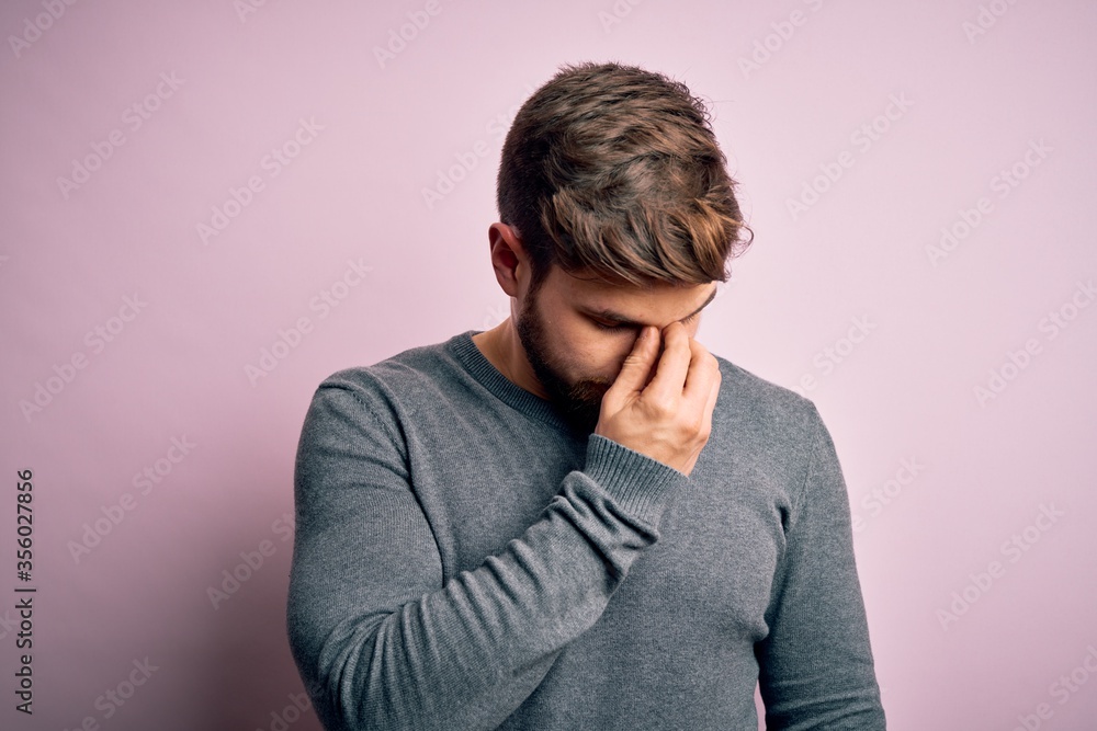 Young handsome blond man with beard and blue eyes wearing casual sweater tired rubbing nose and eyes feeling fatigue and headache. Stress and frustration concept. Young handsome blond man with beard and blue eyes wearing casual sweater tired rubbing nose and eyes feeling fatigue and headache. Stress and frustration concept.
