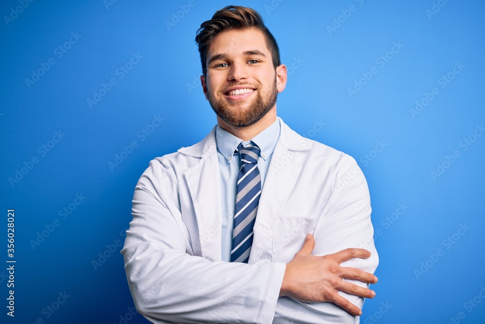 Young blond therapist man with beard and blue eyes wearing coat and tie over background happy face smiling with crossed arms looking at the camera. Positive person. Young blond therapist man with beard and blue eyes wearing coat and tie over background happy face smiling with crossed arms looking at the camera. Positive person.