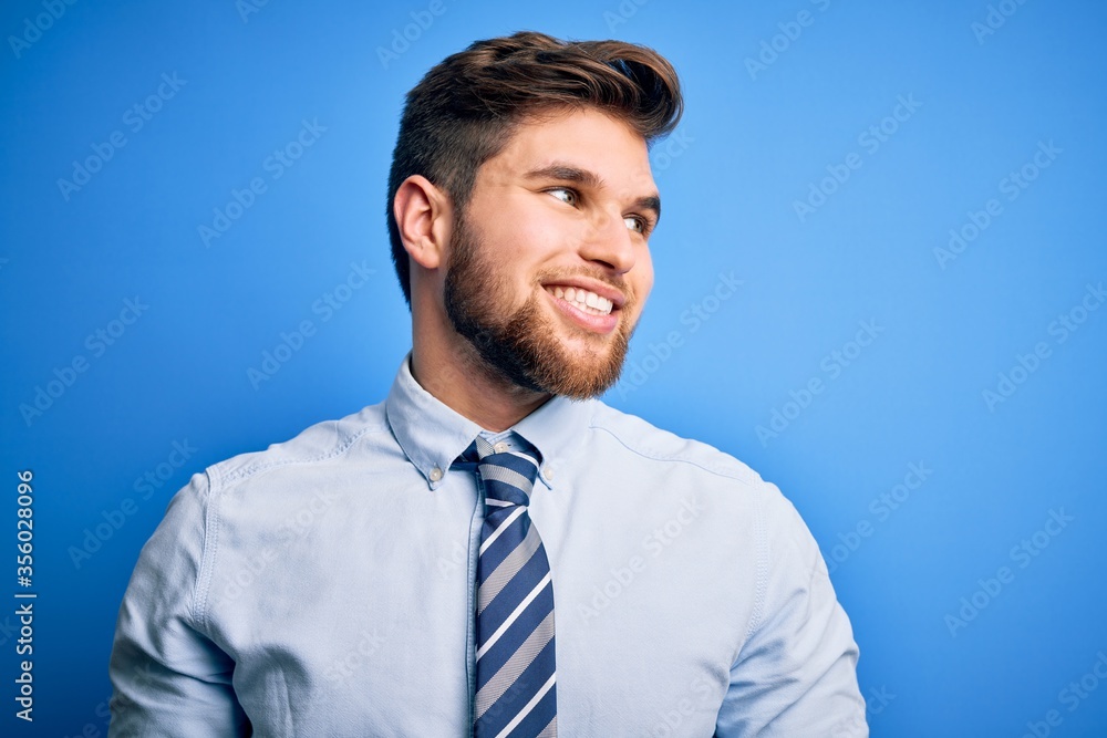 Young blond businessman with beard and blue eyes wearing elegant shirt and tie standing looking away to side with smile on face, natural expression. Laughing confident. Young blond businessman with beard and blue eyes wearing elegant shirt and tie standing looking away to side with smile on face, natural expression. Laughing confident.