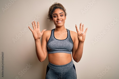 Young african american sportswoman doing sport wearing sportswear over white background showing and pointing up with fingers number nine while smiling confident and happy.