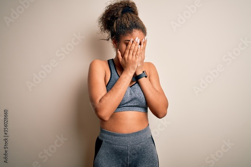 Young african american sportswoman doing sport wearing sportswear over white background with sad expression covering face with hands while crying. Depression concept.