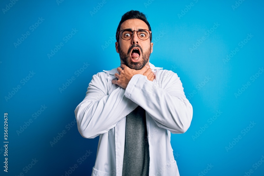 Young handsome doctor man with beard wearing coat and glasses over blue background shouting and suffocate because painful strangle. Health problem. Asphyxiate and suicide concept. Young handsome doctor man with beard wearing coat and glasses over blue background shouting and suffocate because painful strangle. Health problem. Asphyxiate and suicide concept.